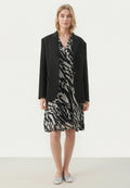 Schwarzer übergroßer Blazer über einem grauen Kleid mit einem schwarzen abstrakten Zebra-Print. Das Modell trägt silberne flache Schuhe. Einfaches, elegantes Design.