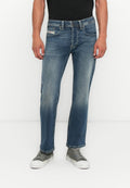 Mann in ausgewaschenen blauen Jeans und grauen Leinenschuhen, der gegen einen weißen Hintergrund steht, mit entspannten Händen an den Seiten.