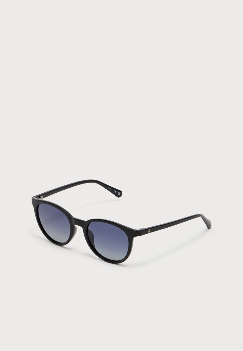 Sonnenbrille mit schwarzem Rahmen, runden Gläsern und blau verlaufenden Gläsern, die auf einer weißen Oberfläche ruhen.