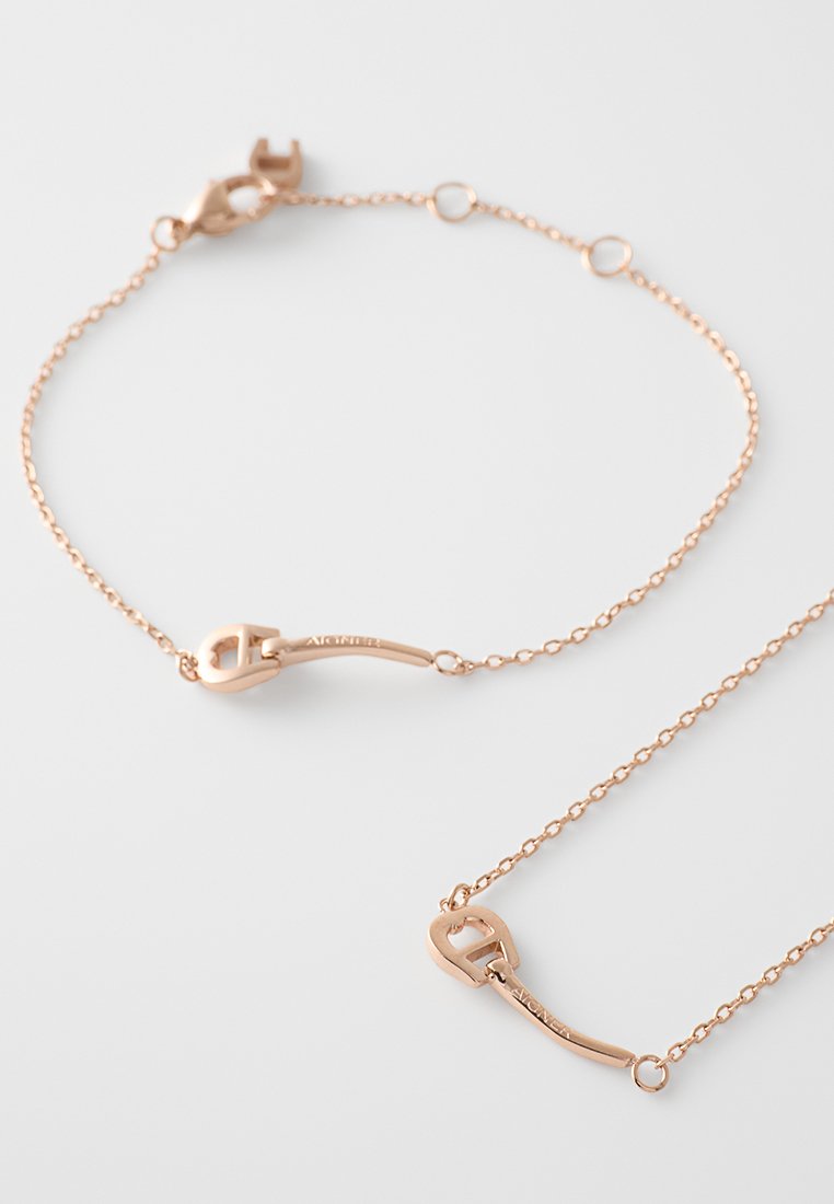 Roségoldarmband mit einem zarten Kettendesign, das einen Verschluss und einen einzigartigen Hakenakzent aufweist. Glatte Textur, minimalistischer Stil.