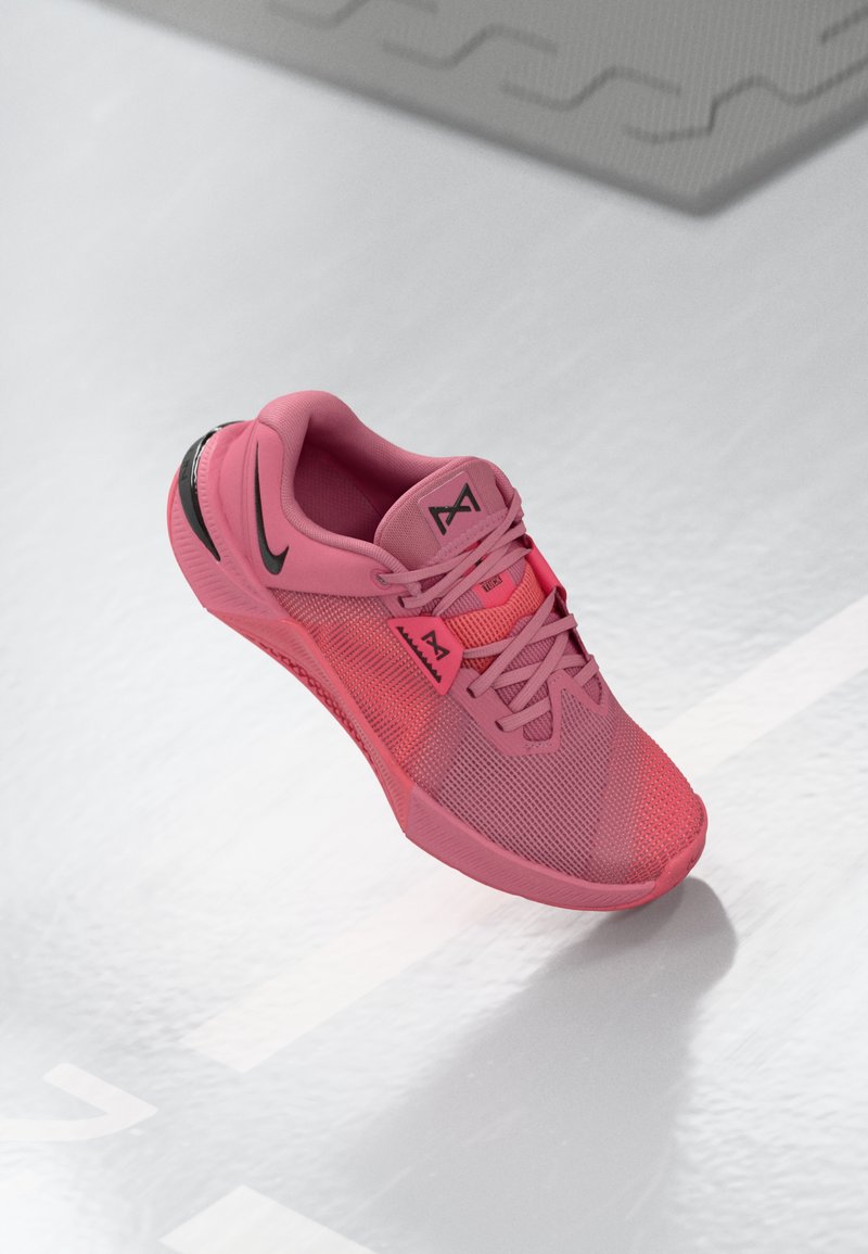 Rosa Sportschuh mit einem Mesh-Obermaterial und schwarzen Akzenten, strukturiertem Sohle und standardmäßiger Schnürung. Leichte Konstruktion ist deutlich erkennbar.
