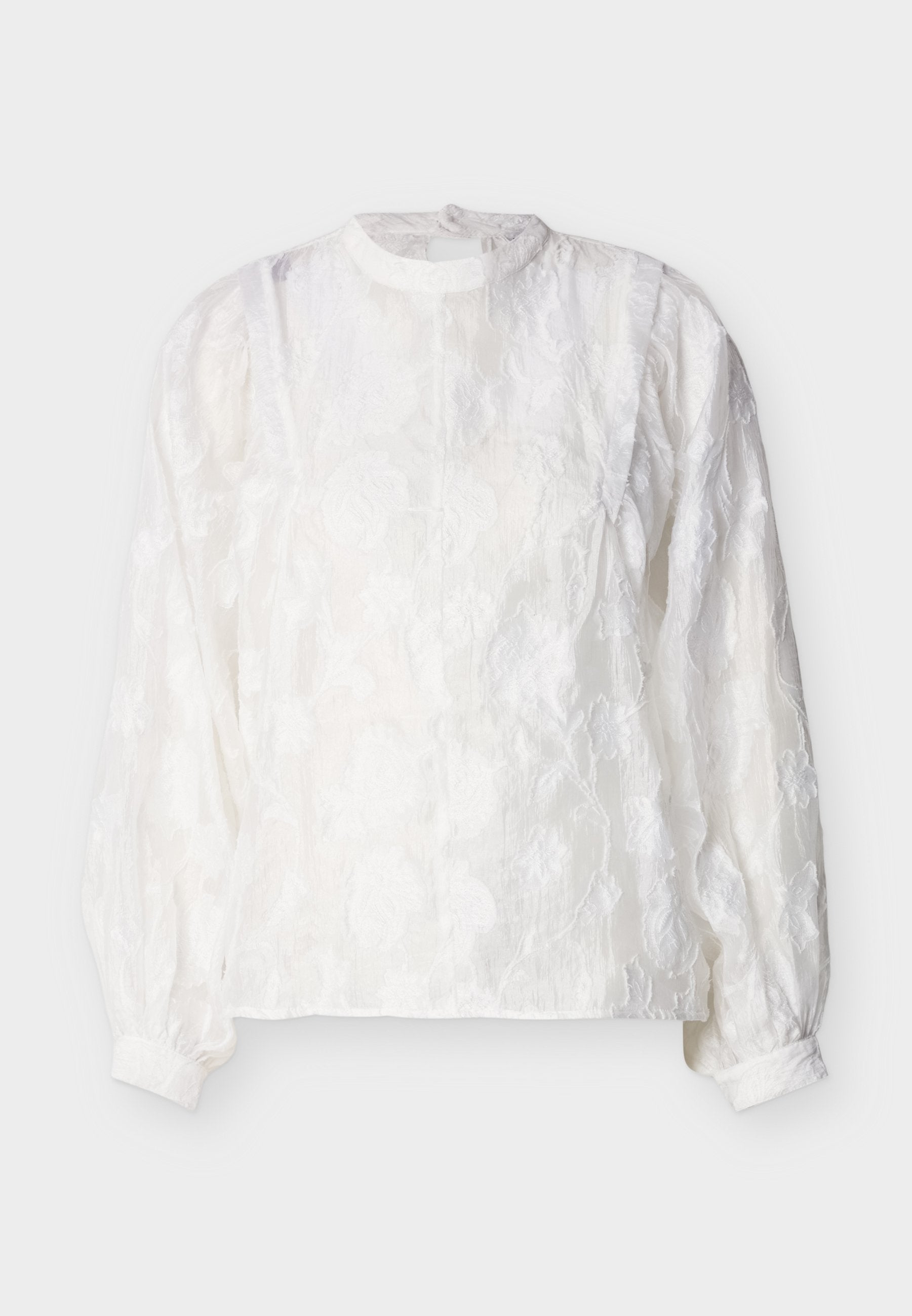 Weiße langärmelige Bluse mit floraler Spitzenstruktur, hohem Kragen, gerafften Puffärmeln und geknöpften Manschetten vor schlichten Hintergrund.