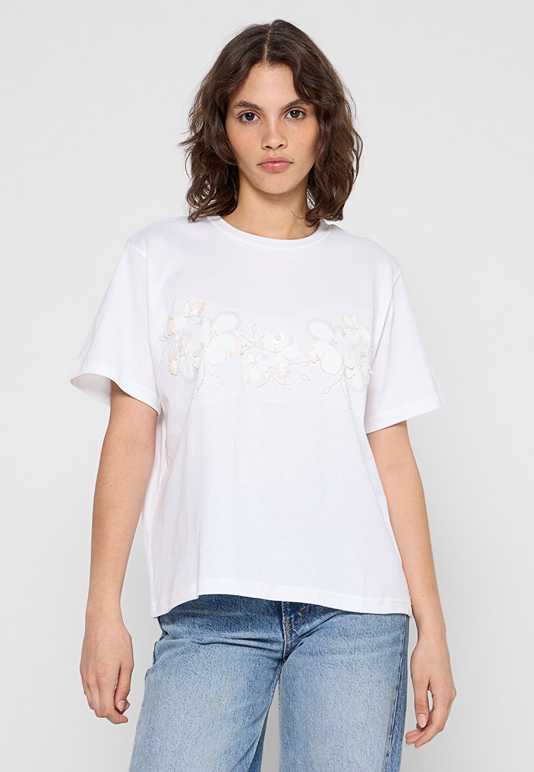Weißes, kurzärmliges T-Shirt aus Baumwolle mit floralen Stickdetails über der Brust, in einem lockeren, kastigen Schnitt.