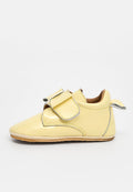 Gelbes Lederschuh für Babys mit glänzender Oberfläche, Klettverschluss, abgerundeter Spitze und hellbraunem Innenfutter. Mit silbernen Nähakzenten.