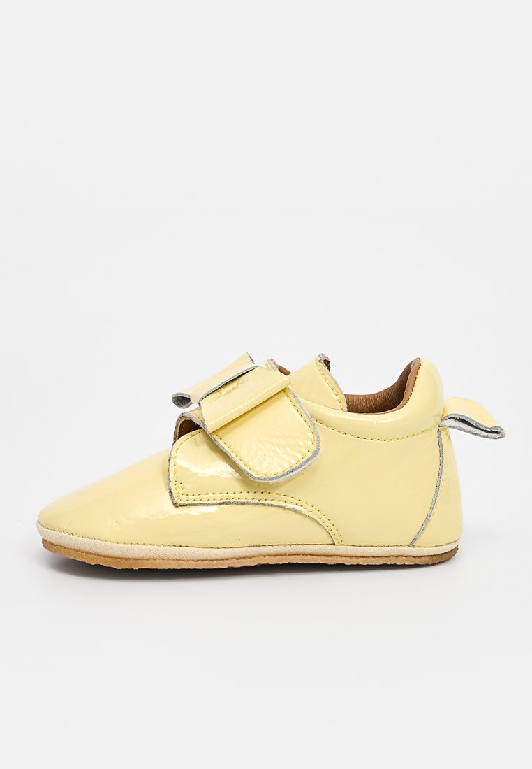 Gelbes Lederschuh für Babys mit glänzender Oberfläche, Klettverschluss, abgerundeter Spitze und hellbraunem Innenfutter. Mit silbernen Nähakzenten.