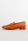 Oranger Lederloafer mit flachem Absatz, ausgestattet mit einem dekorativen goldenen Schnallendetail und einer glatten Textur. Runde Zehenpartie und minimalistisches Design.