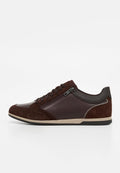 Dunkelbrauner Sneaker mit niedrigem Schaft, vorne mit Schnürung und seitlichem Reißverschluss, kombiniert aus Leder- und Wildlederpaneelen, beige Zwischensohle und schwarze Außensohle.