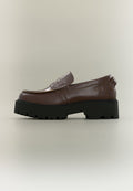 Brauner Leder-Slipper mit dicker schwarzer Profilsohle und aufgenähten Details auf neutralem Hintergrund.
