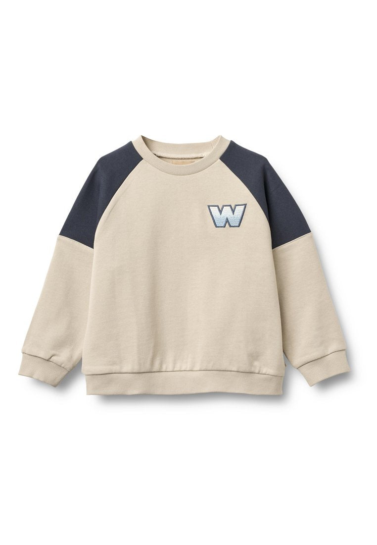 Beiger Pullover mit marineblauen Raglanärmeln, gerippten Bündchen und Saum. Verziert mit einem dekorativen, gestickten Buchstaben "W" auf der Brust.