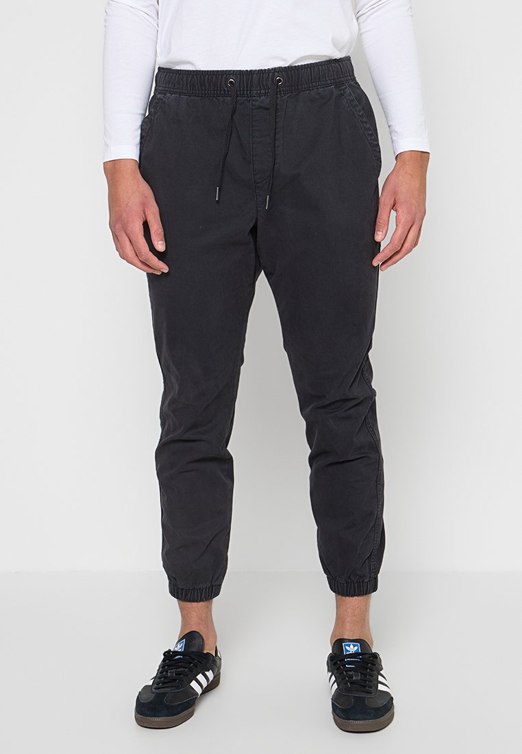 Schwarze Jogginghosen aus Baumwolle mit elastischem Bund und Kordelzug. Verjüngte Beine mit elastischen Bündchen. Getragen mit schwarzen Turnschuhen.