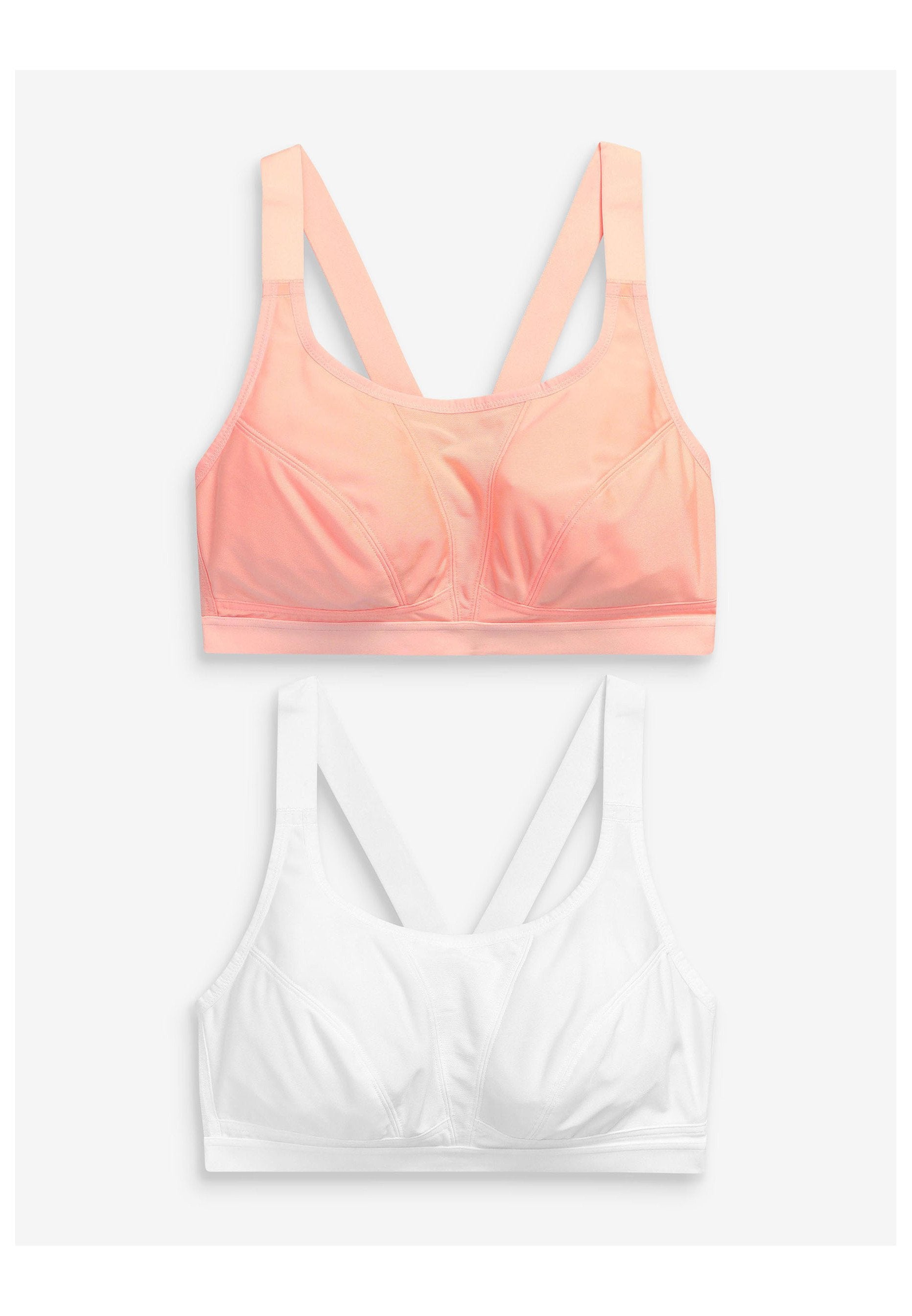 Zwei Soft-Cup-BHs mit breiten Trägern und Racerback-Design, einer in Korallenpink und einer in Weiß, flach auf einem hellen Hintergrund präsentiert.