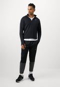 Mann in schwarzem und grauem Sportanzug mit weißen Socken und schwarzen Turnschuhen, der vor einem schlichten weißen Hintergrund steht.