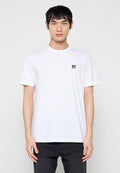 Weißes Baumwoll-T-Shirt mit kurzen Ärmeln, Rundhalsausschnitt und einem kleinen schwarzen Diesel-Logo-Patch auf der linken Brust. Kombiniert mit dunklen Jeans.