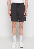 Mann trägt dunkelgraue Shorts mit Kordelzug, weiße Sportsocken und weiße Sneakers, steht vor neutralem Hintergrund.