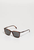 Braune Schildpatt-Sonnenbrille mit quadratischer Form, dunkelgrauen Gläsern und Metallakzenten an den Bügeln. Glatte Oberfläche und elegantes Design.