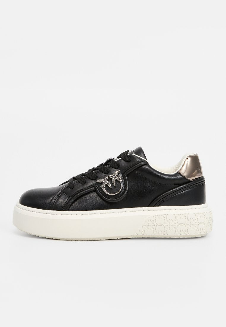 Schwarze Ledersneaker mit rundem Emblem, Schnürdesign und dicker weißer Sohle mit strukturierten Akzenten. Metallisches Detail an der Ferse.