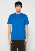 Blaues Baumwoll-T-Shirt mit rundem Halsausschnitt, kurzen Ärmeln und einem kleinen roten Logo-Patch auf der linken Brustseite. Glatte Textur.