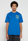 Blaues Baumwoll-T-Shirt mit kurzen Ärmeln, rundem Halsausschnitt und einem grafischen Aufdruck in gelbem Text auf der linken Seite. Kombiniert mit dunkler Hose.