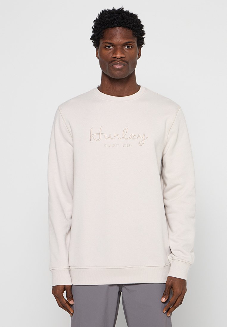 Hellbeige Sweatshirt mit Rundhalsausschnitt, gerippten Bündchen und dem gestickten "Hurley Surf Co."-Logo in einem etwas dunkleren Farbton. Glatte Textur.