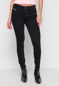 Frau trägt schwarze Skinny-Jeans und schwarze spitze Stiefeletten, steht vor einem weißen Hintergrund.