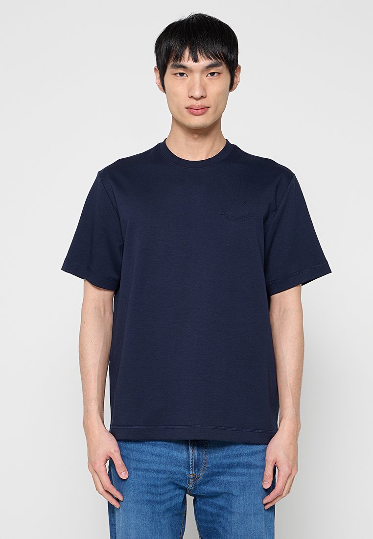 Marineblaues Baumwoll-T-Shirt mit Rundhalsausschnitt, kurzen Ärmeln und einem dezenten Logo. Kombiniert mit blauen Jeans aus Denim. Glatte Textur.