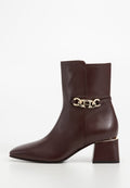 Braune Leder-Ankle-Boots mit spitzer Zehenpartie, goldener Kettenakzent am Knöchel und quadratischem Blockabsatz. Glatte Textur und elegantes Design.