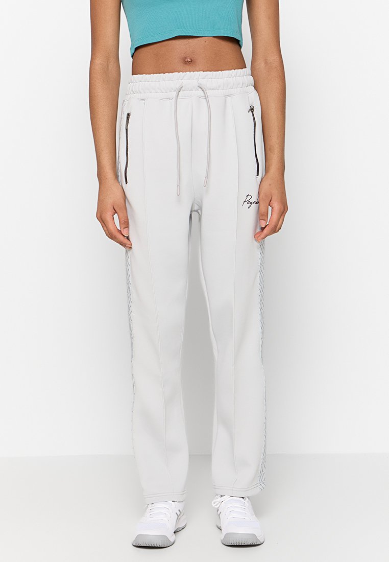 Weiße Jogginghose mit elastischem Bund, Reißverschlusstaschen und strukturierten seitlichen Akzenten. Kombiniert mit einem türkisfarbenen Cropped-Top und weißen Sneakers.