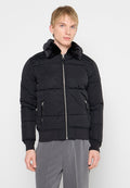 Schwarze Steppjacke mit einem Kragen aus Kunstfell, durchgehendem Reißverschluss und seitlichen Taschen. Besitzt eine gesteppte Textur sowie gerippte Bündchen und Saum.