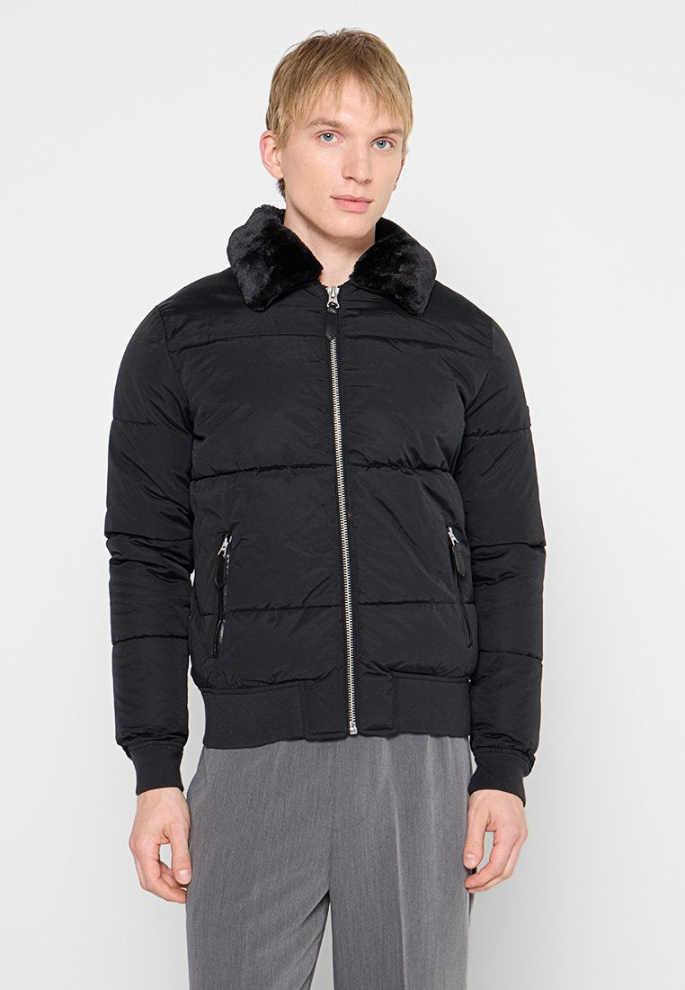 Schwarze Steppjacke mit einem Kragen aus Kunstfell, durchgehendem Reißverschluss und seitlichen Taschen. Besitzt eine gesteppte Textur sowie gerippte Bündchen und Saum.