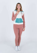 Rosa-weiße Kapuzenjacke mit Reißverschluss und einer türkisfarbenen Tasche, kombiniert mit passenden rosa Leggings. Das Model trägt weiße Sneakers. Glatte Stofftextur.