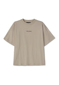 Beige Baumwoll-T-Shirt mit Oversize-Schnitt, kurzen Ärmeln, rundem Halsausschnitt und zentriertem schwarzen Text "PEGADOR." Keine Muster oder zusätzlichen Details.