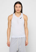 Mann mit langen schwarzen Haaren, der ein ärmelloses weißes Nike-Sportoberteil und hellgraue Shorts mit Kordelzug trägt, frontal vor einem einfarbigen Hintergrund.