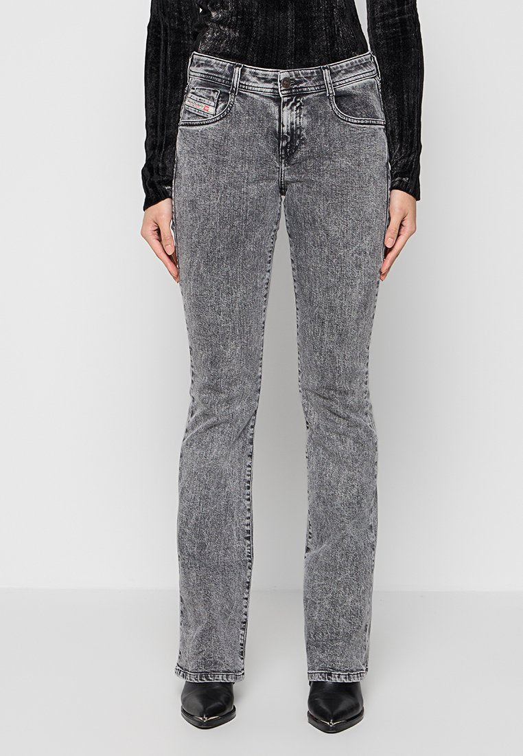 Eine Person trägt hochtaillierte, graue Acid-Wash-Jeans mit geraden Beinen, schwarze Stiefeletten mit spitzem Fuß und ein langärmliges schwarzes Oberteil.