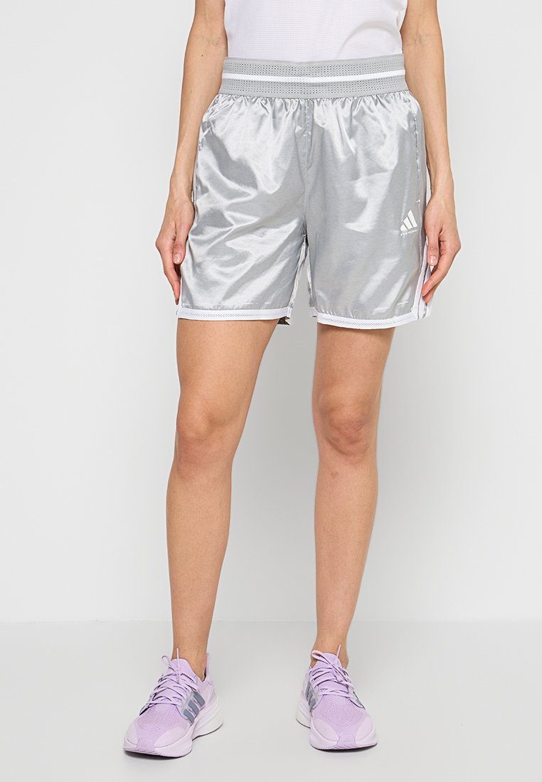Silberne Sportshorts mit elastischem Bund, seitlichen Akzenten und kontrastierendem weißen Rand. Kombiniert mit hellvioletten Sportschuhen.