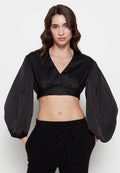 Schwarze, cropped Bluse mit tiefem V-Ausschnitt und dramatischen Ballonärmeln. Hergestellt aus glattem, glänzendem Stoff und mit taillierter Taille.