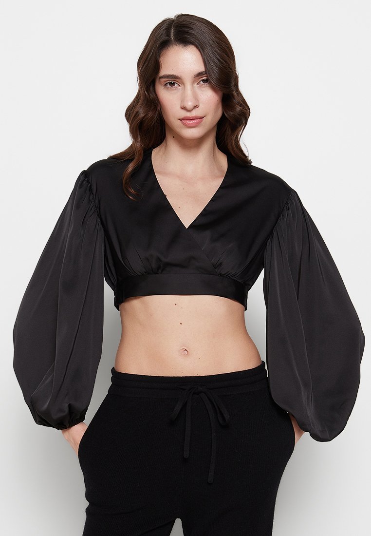 Schwarze, cropped Bluse mit tiefem V-Ausschnitt und dramatischen Ballonärmeln. Hergestellt aus glattem, glänzendem Stoff und mit taillierter Taille.