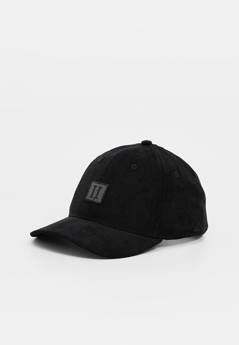 Schwarze Cordura-Baseballmütze mit strukturierter Oberfläche, gebogenem Schirm und einem quadratischen Logo-Patch auf der Vorderseite. Verfügt über dunkle Nähte und Belüftungslöcher.