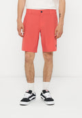 Mann trägt korallenfarbene knielange Shorts, weiße Socken und schwarz-weiße Turnschuhe, steht vor einem schlichten weißen Hintergrund.