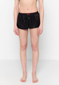 Frontalansicht einer Person, die schwarze Satin-Boxershorts von Diesel mit elastischem Bund und einer Einzelknopfdetails trägt und barfuß vor einer weißen Wand steht.