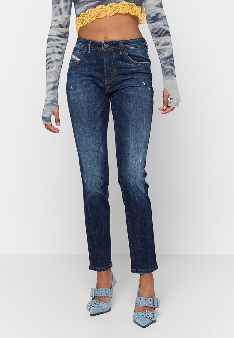 Dunkelblaue Denim-Jeans mit Slim-Fit, leichten Verwaschungen, fünf Taschen und Stichdetails. Kombiniert mit hellblauen Absatzschuhen.