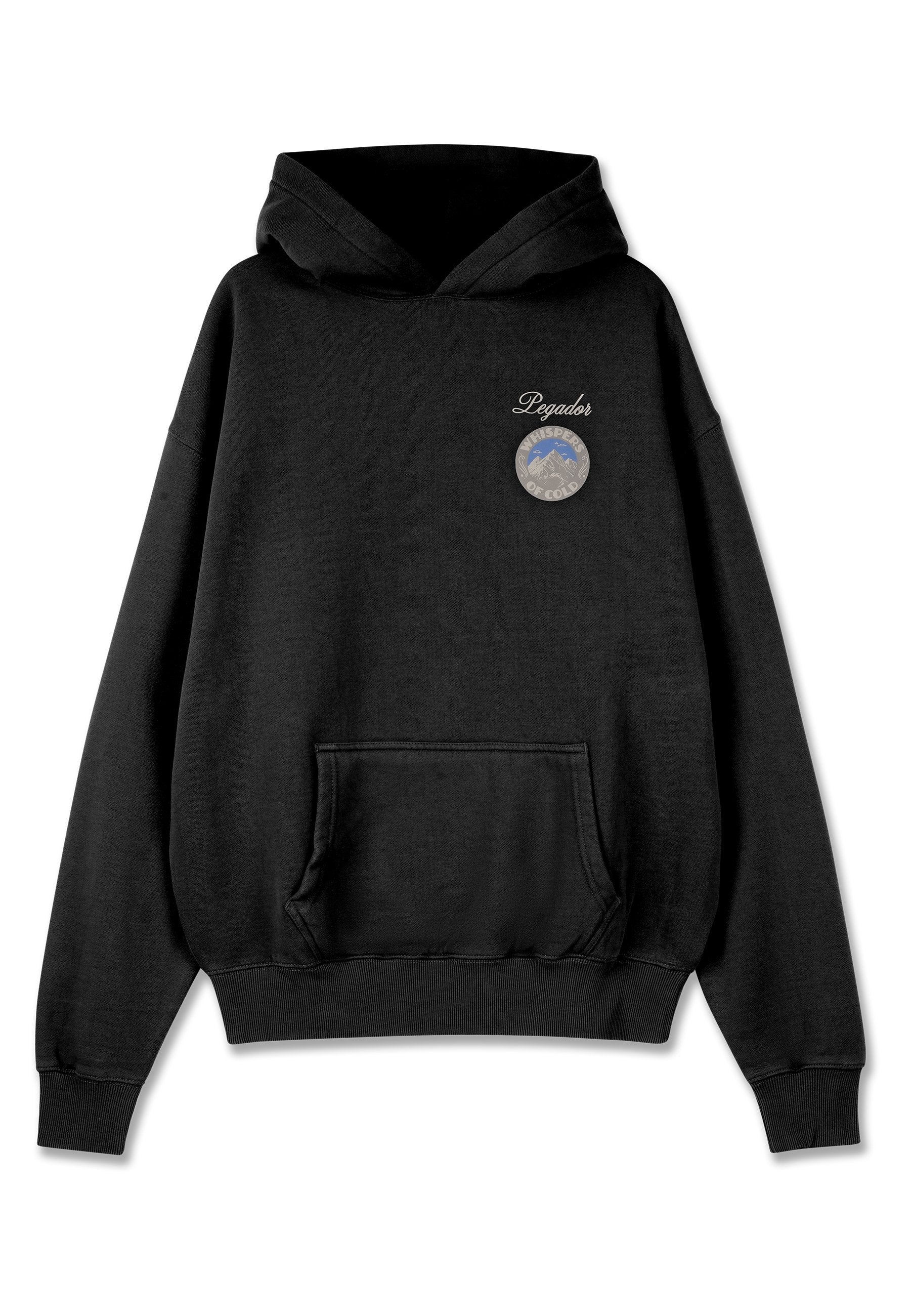 Schwarzer Kapuzenpullover mit frontaler Tasche, der ein rundes Patch auf der Brust mit Bergmotiven und Text zeigt. Weicher Stoff, lässiges Design.