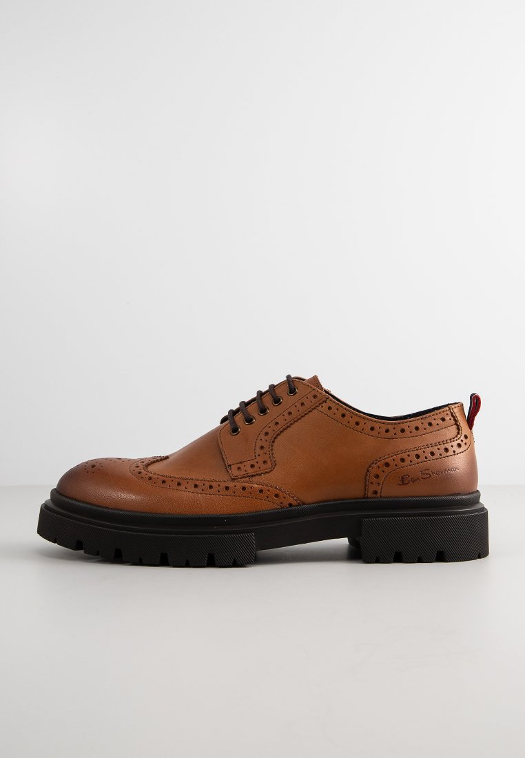 Braune Leder Schuhe mit Brogue-Details, runder Zehenpartie und schwarzer Gummisohle. Verfügt über fünf Ösen und eine rote Zuglasche auf der Rückseite.