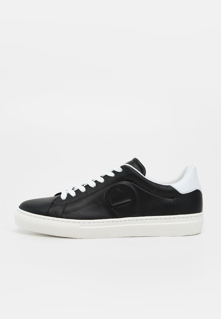 Schwarzer flacher Ledersneaker mit weißen Schnürsenkeln, weißer Sohle und weißer Fersenlasche, mit einem dezent eingeprägten Logo an der Seite.
