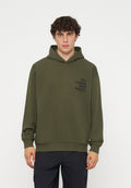 Junger Mann mit lockigem Haar trägt einen olivgrünen Hoodie mit schwarzem Schriftzug „The Future Surf Society“ auf der linken Brust und schwarze Hose.