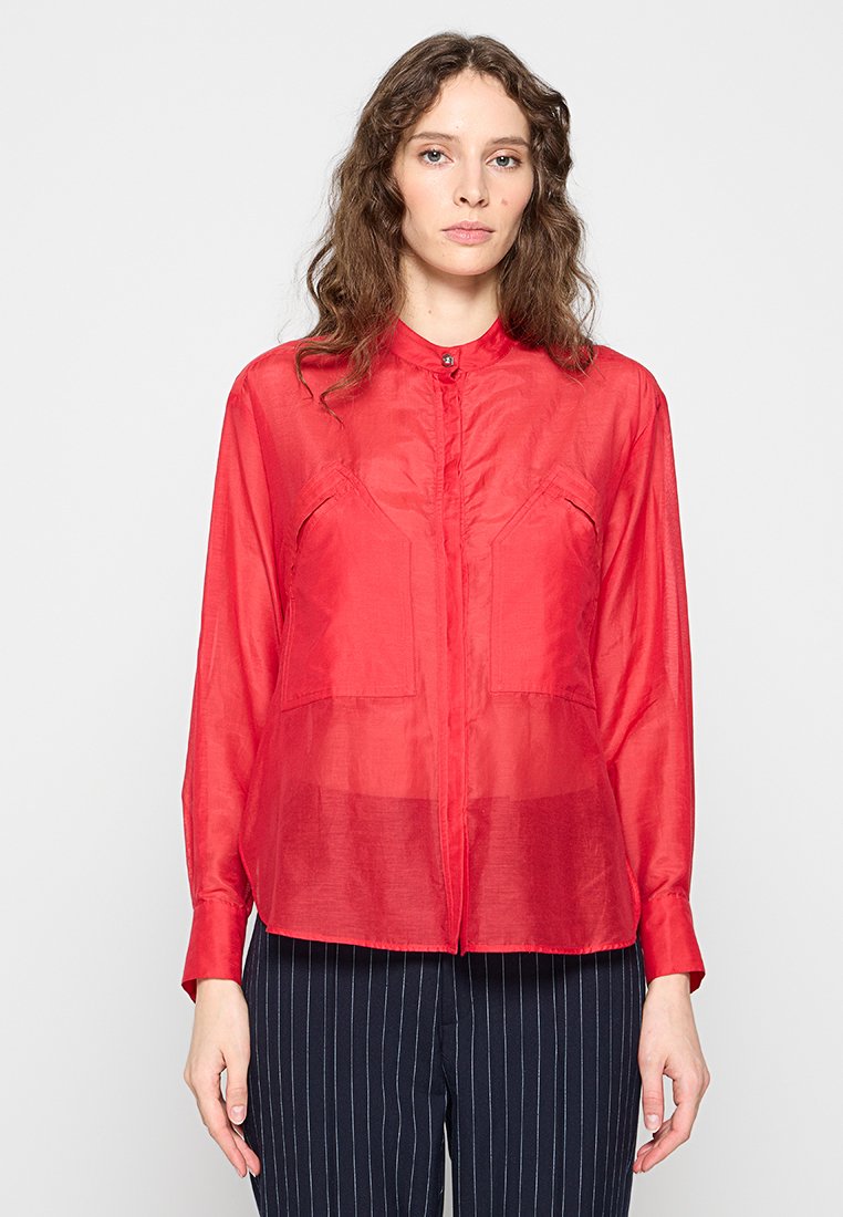 Rote, leicht durchscheinende Bluse mit durchgehendem Knopfverschluss, Kragen und zwei Brusttaschen. Lange Ärmel mit geknöpften Manschetten.
