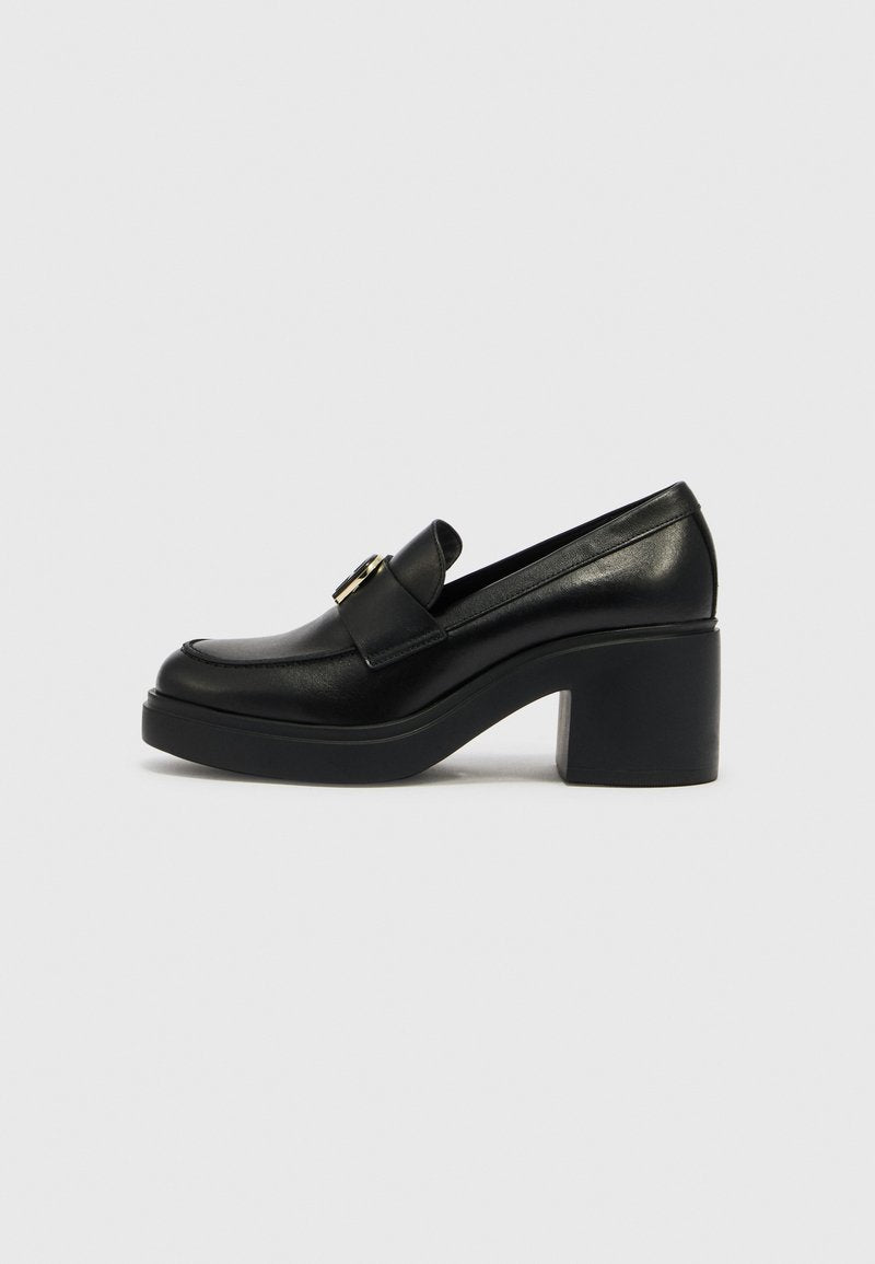 Schwarzer Leder-Slipper mit hohem Absatz, klobigem Absatz und goldener Schnallenverzierung auf dem Spann, im Profil vor hellgrauem Hintergrund gezeigt.