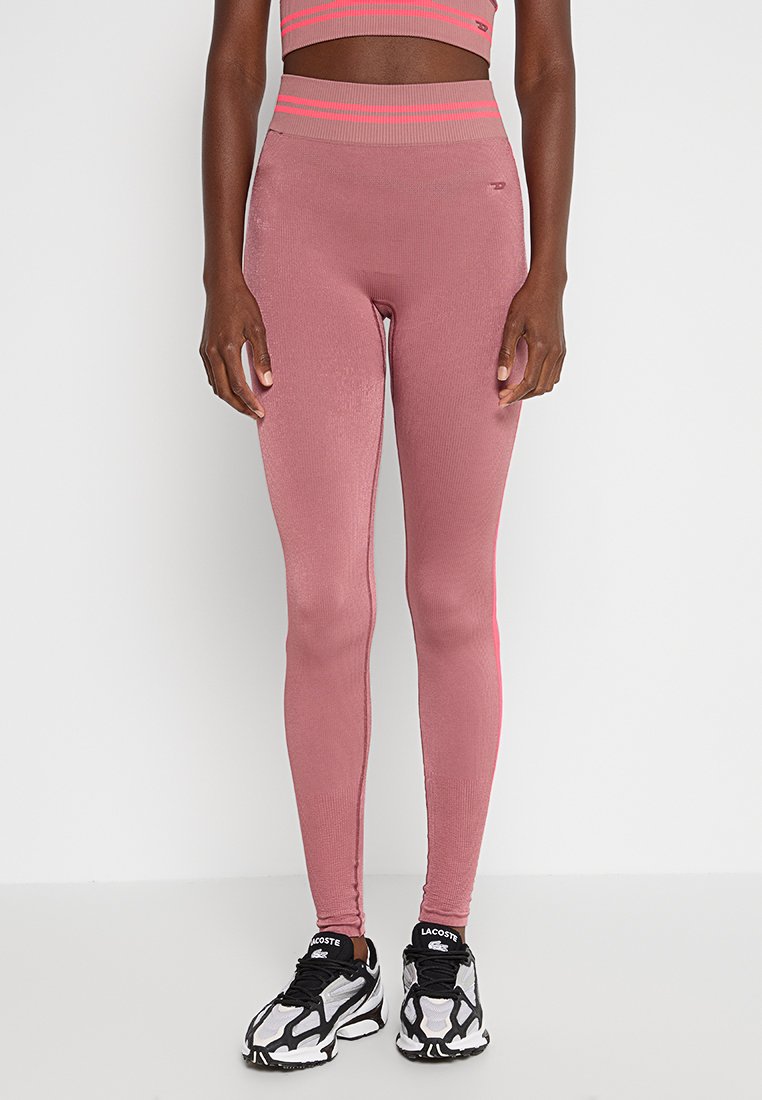 Hochtaillierte pinke Leggings mit geripptem Muster und neonfarbenen Akzenten, kombiniert mit schwarz-weißen Sportschuhen.