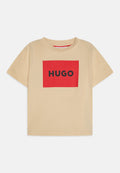 Beige Baumwoll-T-Shirt mit kurzen Ärmeln, das ein großes rotes rechteckiges Design und den schwarzen Text "HUGO" in der Mitte auf der Vorderseite zeigt.
