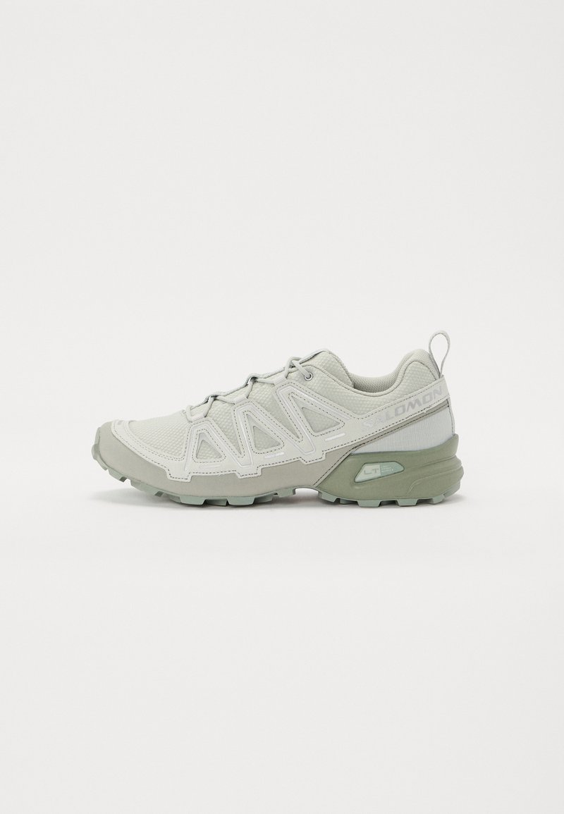 Helle graue Sportschuhe mit Mesh-Obermaterial, strukturiertem Design und grünen Akzenten. Verfügt über eine Zuglasche und eine robuste Laufsohle für besserer Traktion.