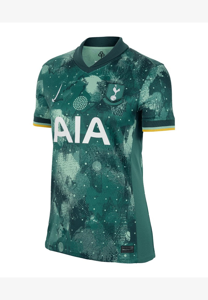 Grünes Fußballtrikot mit einem strukturierten Muster aus Punkten und abstrakten Formen. Es hat einen Kragen, kurze Ärmel und ein Logo auf der Brust.